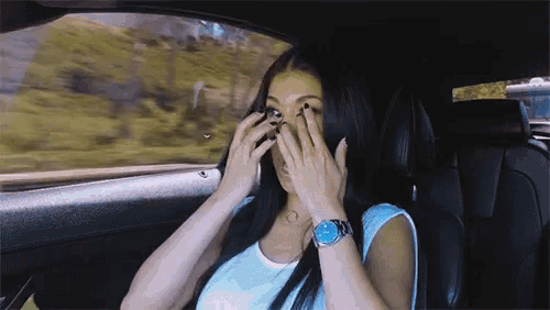 a woman wearing a watch is covering her eyes while sitting in a car