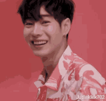 a close up of a young man wearing a pink and white shirt and smiling .
