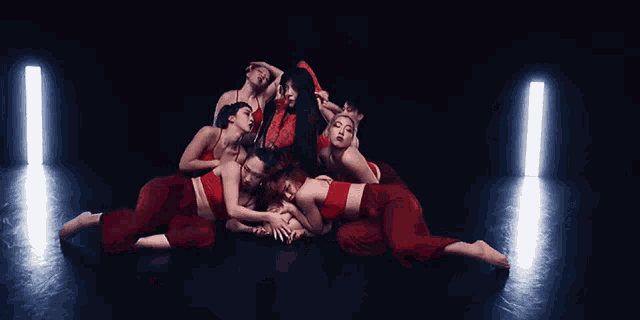 a group of women in red dresses are laying on the floor in a dark room