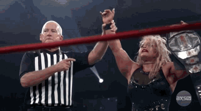 a referee points to a woman in a wrestling ring with axstv written on the bottom right
