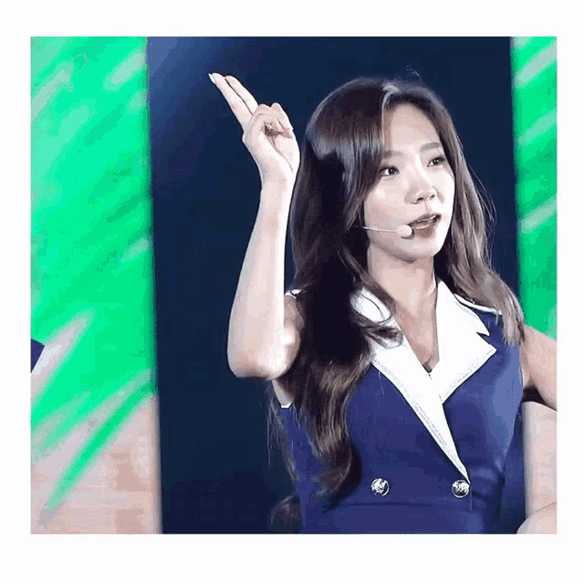 a woman in a blue and white dress is singing into a microphone and making a gesture with her hand
