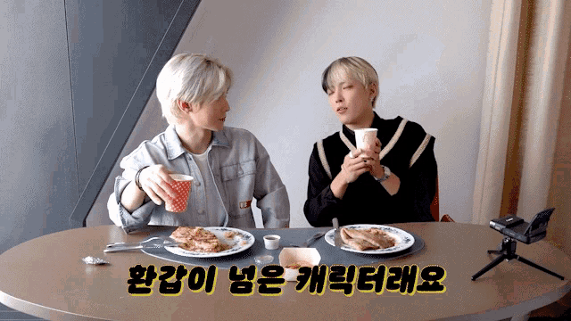 two young men are sitting at a table with plates of food and cups of coffee with a caption in korean