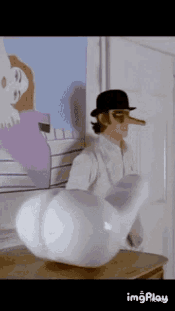 a man with a long nose and a hat is standing next to a large white object on a table .