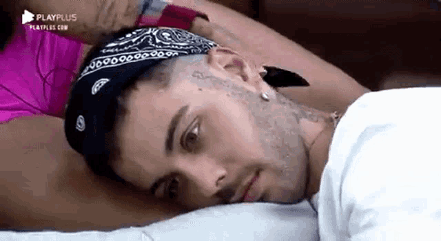 a man with a bandana on his head is laying on a bed next to a woman .