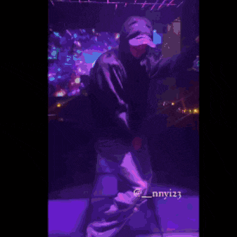 a person in a hoodie is dancing on a stage in a dark room .