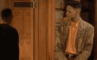 a man in a jacket and orange shirt is standing in front of a door .