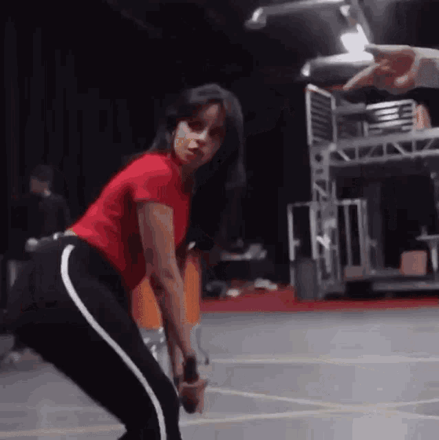 a woman in a red shirt and black pants is squatting on a stage while holding a microphone .