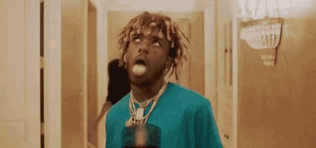a man with dreadlocks and a blue shirt is standing in a hallway with his tongue out .