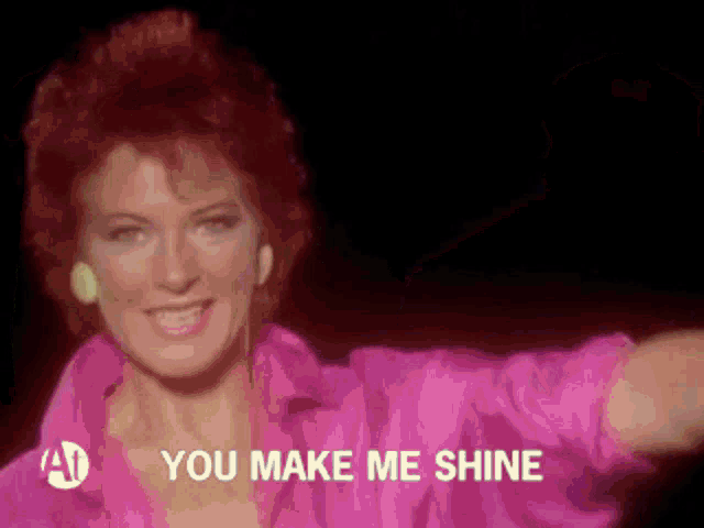 a woman in a pink shirt is singing the song you make me shine .