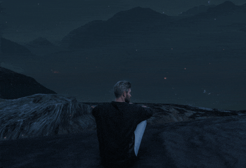 a man in a black shirt sits on a rock at night