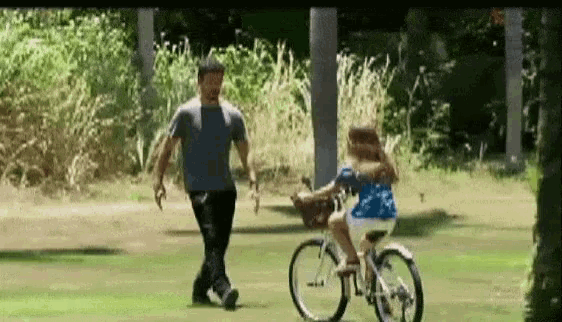 a man is helping a little girl ride a bike in the park .