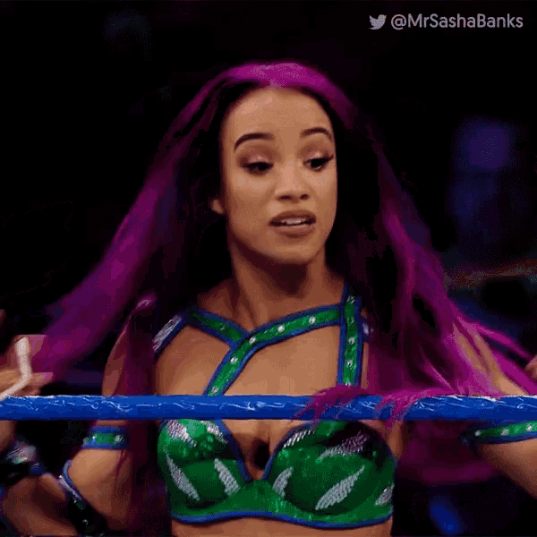 a woman with purple hair is standing in a wrestling ring with her hands in the air .