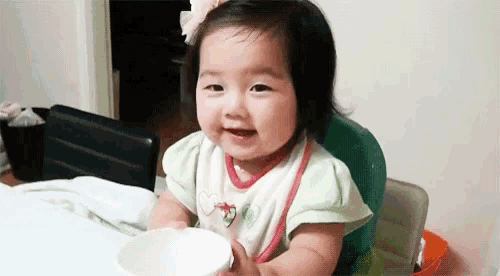 a baby girl is sitting in a high chair holding a white bowl and smiling .