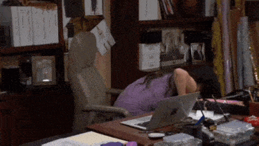 a woman in a purple dress is sitting at a desk in front of a laptop