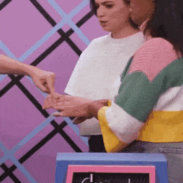 a woman in a colorful sweater is holding another woman 's hand and pointing at it .