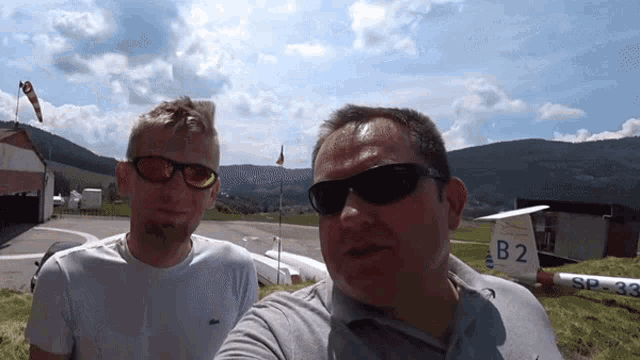 two men taking a selfie in front of a plane with the number b2 on it