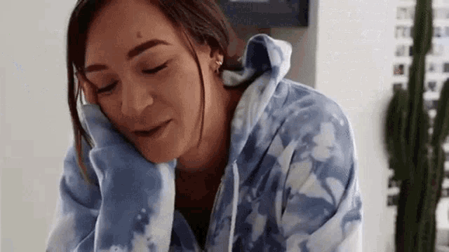 a woman wearing a blue tie dye hoodie is sitting at a table with her head on her hand .