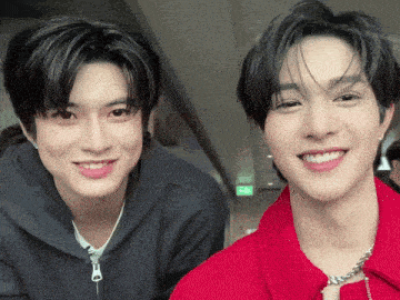 two young men are posing for a picture together and one is wearing a red jacket