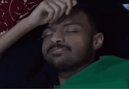 a man with a beard and a green shirt is laying down with his eyes closed