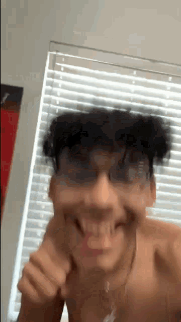 a shirtless man is making a funny face in front of a window with blinds .