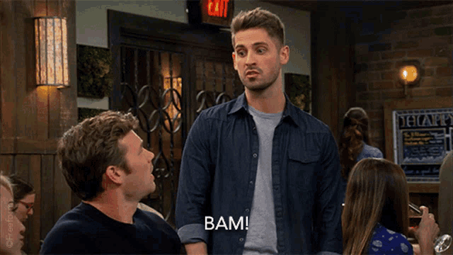 a man in a blue shirt says bam in front of a sign that says exit