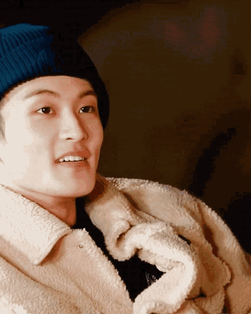 a man wearing a blue beanie and a white jacket smiles