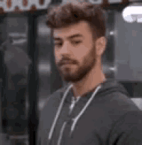 a man with a beard and a hoodie is standing in front of a building .