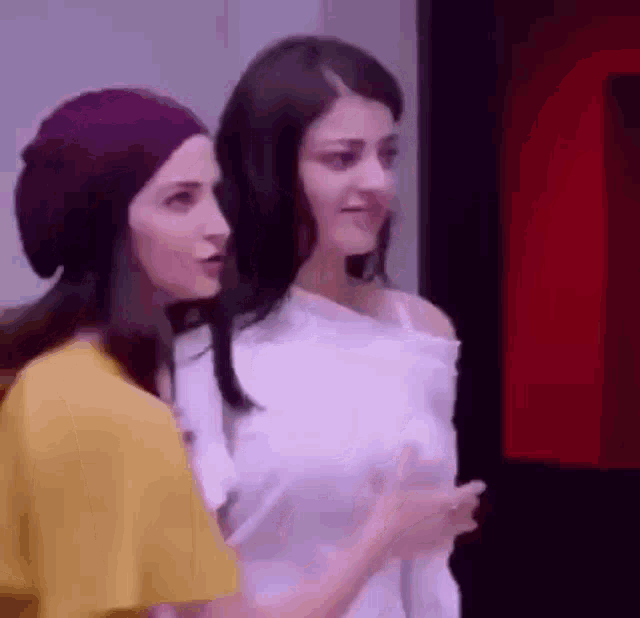 two women are standing next to each other and talking to each other . one of the women is wearing a purple hat .