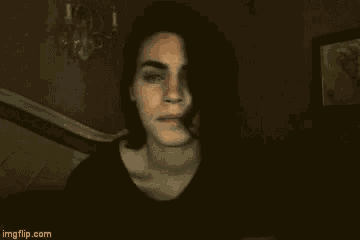 a young man with long dark hair is sitting on a bed .