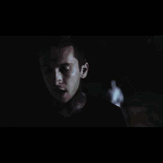a man with a tattoo on his arm is standing in a dark room with a green light behind him
