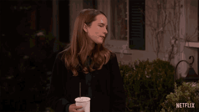 a woman is holding a cup with a straw in front of a netflix sign