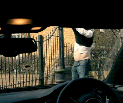 a man with a very large belly is standing in front of a fence in a car