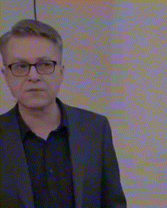 a man wearing a suit and glasses is standing in front of a white wall .
