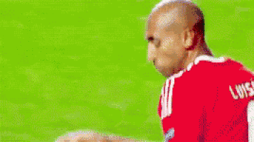 a man in a red shirt is standing in front of a green field .