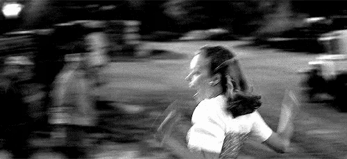 a black and white photo of a young girl running down a street .