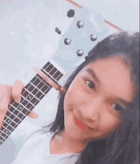 a young girl is holding a ukulele in her hand and smiling .