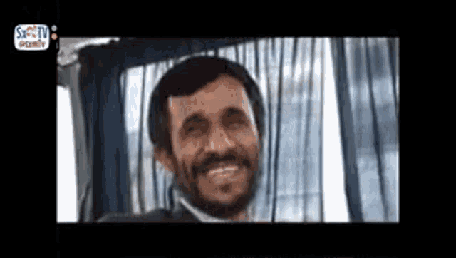 a man with a beard is smiling while sitting in a car .