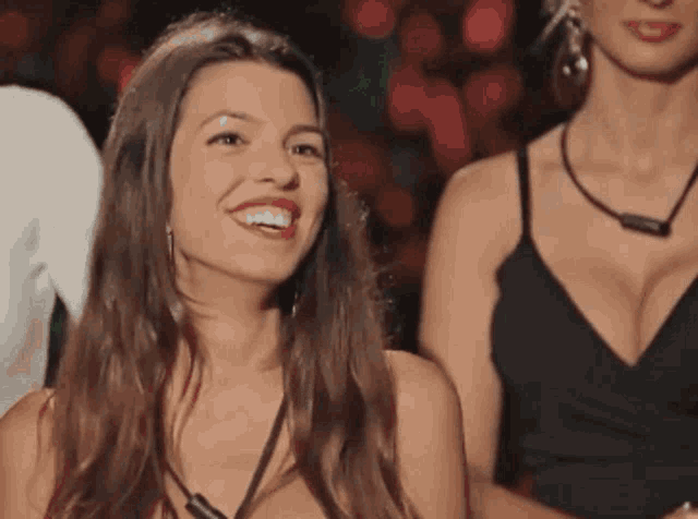 a woman in a black dress is smiling in front of a group of people