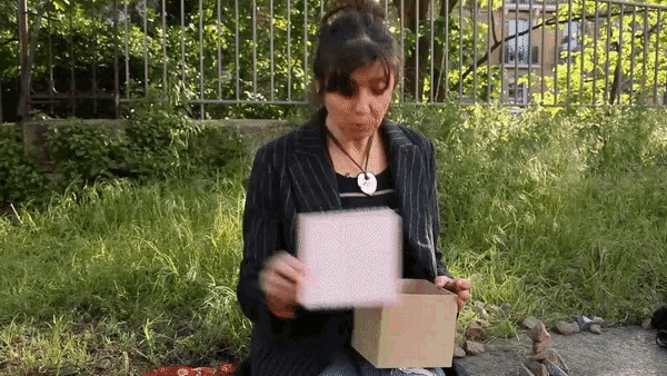 a woman is sitting in the grass holding a cardboard box and a piece of paper