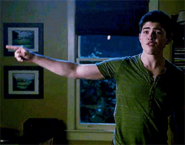a young man in a green shirt is pointing at the camera .