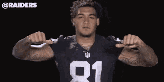 a man in a raiders jersey is flexing his muscles and pointing at himself .