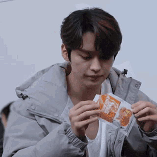 a young man in a grey jacket is holding a bag of orange juice