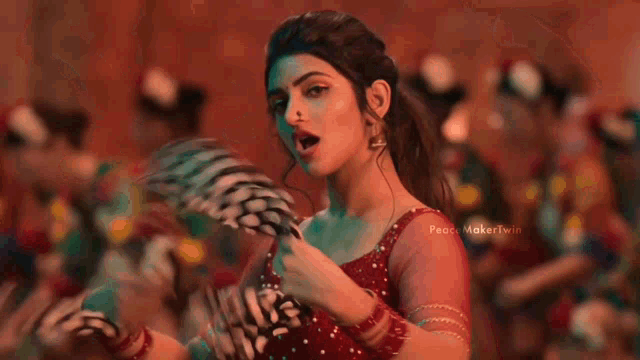 a woman in a red dress is holding a feather in her hand and looking at the camera .