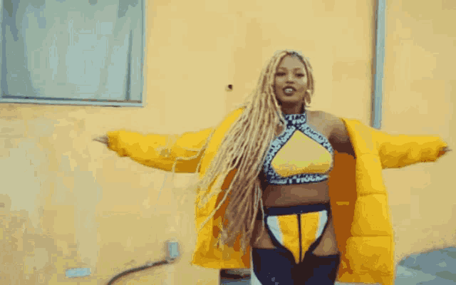 a woman with dreadlocks wearing a yellow jacket and a yellow top with the word moschino on the collar