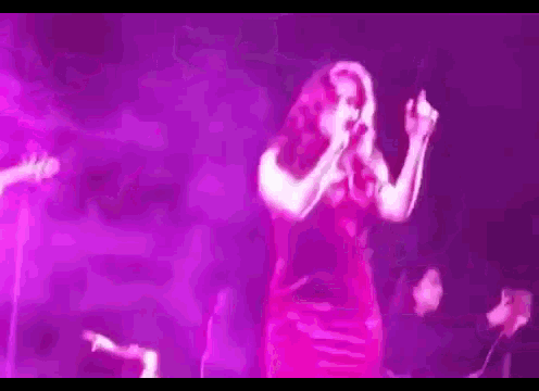 a woman in a red dress is singing into a microphone on a stage in front of a crowd .