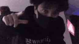 a man wearing a mask is pointing at the camera while wearing a black hoodie .