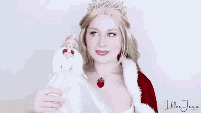 a woman is wearing a tiara and holding a barbie doll .