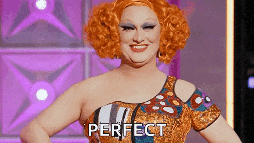 a drag queen with red hair and a leopard print dress is smiling and says perfect