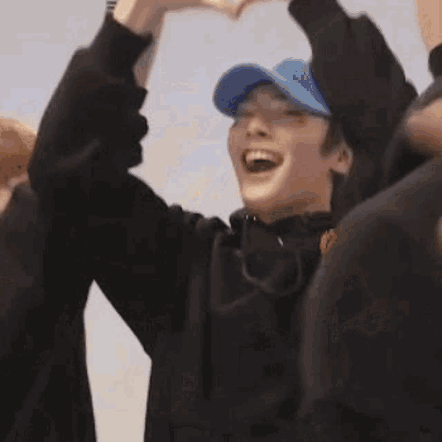 a man is making a heart shape with his hands while wearing a blue hat .