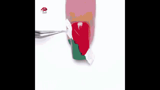 a close up of a person 's nails being painted with red , green and white nail polish .